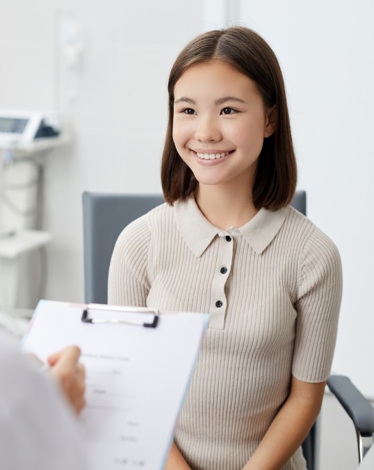 Young woman smiling while her dentist writes on a clipboard
