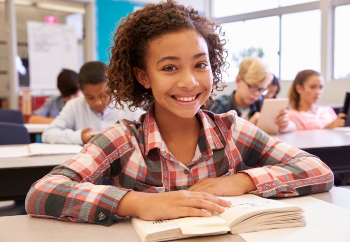 Smiling young girl sitting at school desk after children's dentistry in Saint Peters