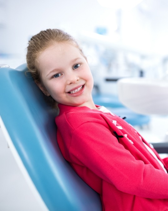 Young girl in red jacket smiling in dental chair