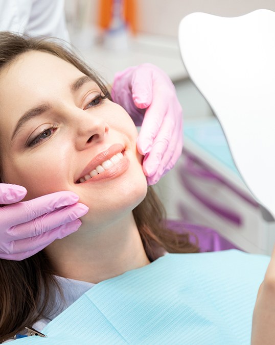Woman in dental chair smiling at reflection with dentist’s hands by her face