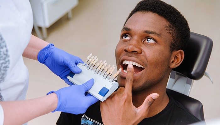 Man touching his teeth as dentist holds shade guide to his smile