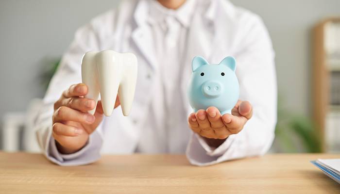 Chin-down view of dentist in white coat at desk holding large model tooth and piggy bank