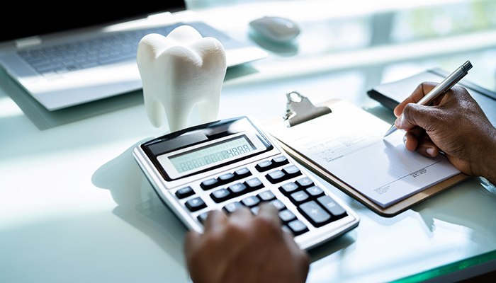 Someone calculating costs with a calculator and pen and paper next to large tooth on a desk