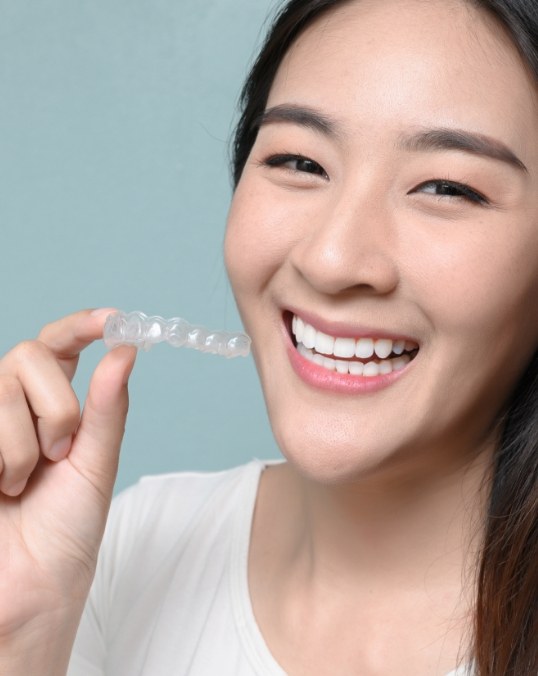 Smiling young woman holding Invisalign clear aligner