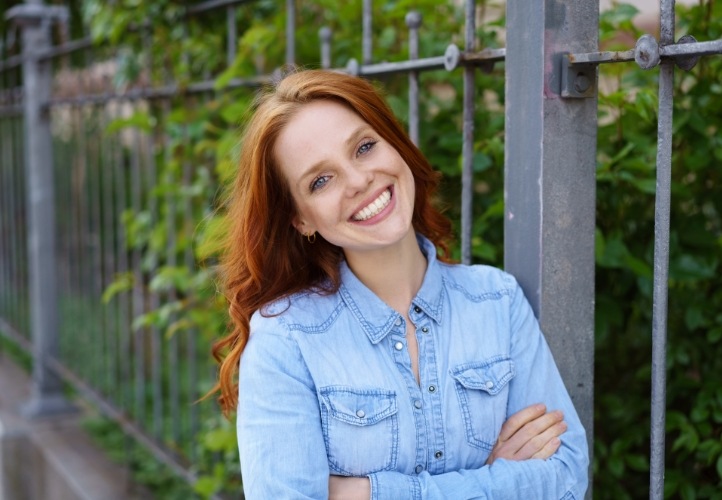 Smiling redheaded woman in denim shirt with dental crowns and bridges in Saint Peters