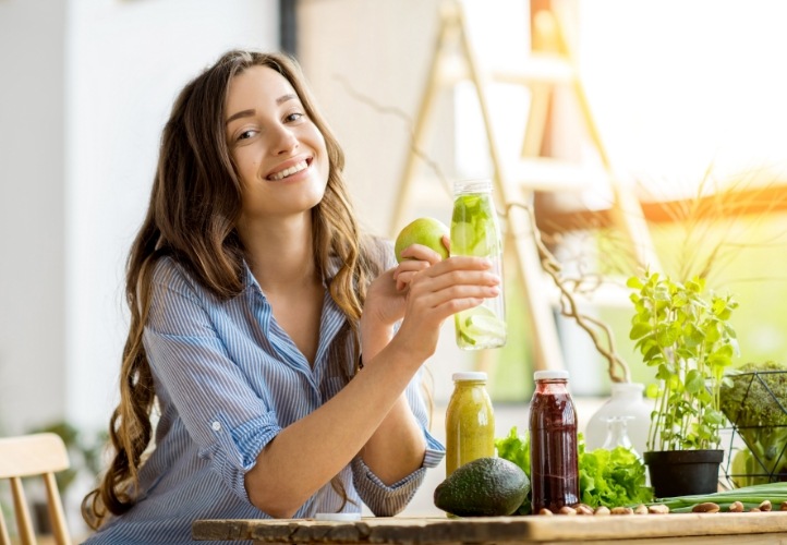 Smiling young woman with dental implants in Saint Peters holding an apple and fruit juice