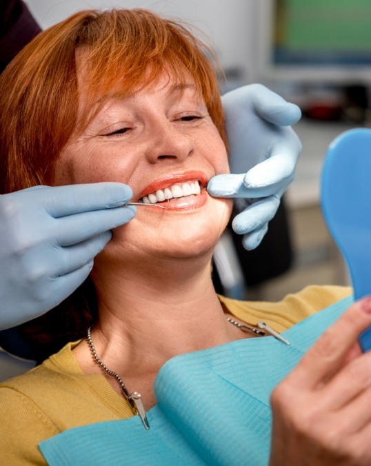 Older redheaded woman seeing her smile in mirror in dental chair