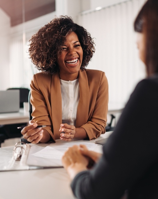 Businesswoman laughing with person sitting across desk from her