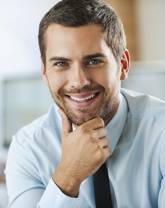 Smiling man in dress shirt and tie with his hand on his chin