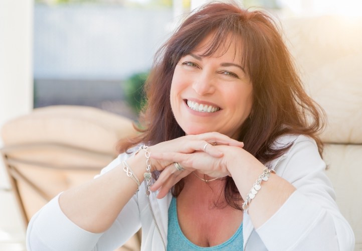 Woman in white blouse smiling with implant dentures in Saint Peters