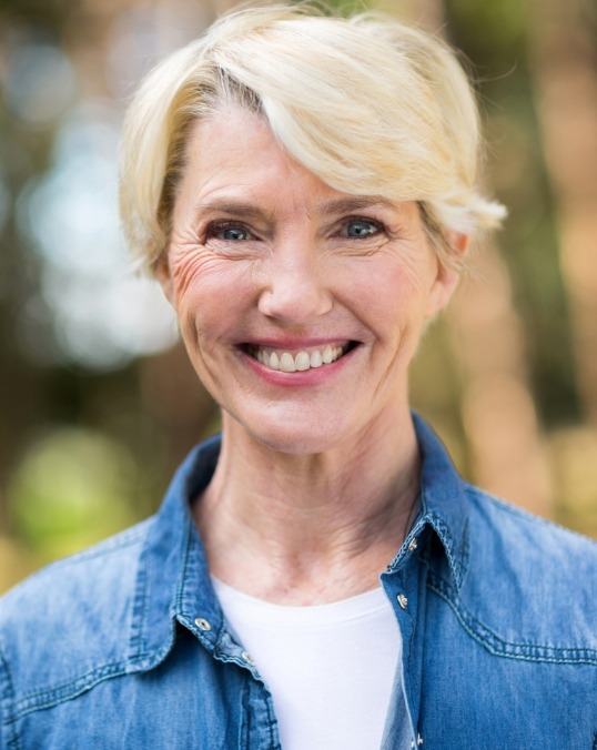 Older blonde woman in denim shirt smiling outdoors