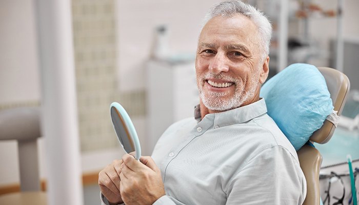 man smiling while holding dental mirror 