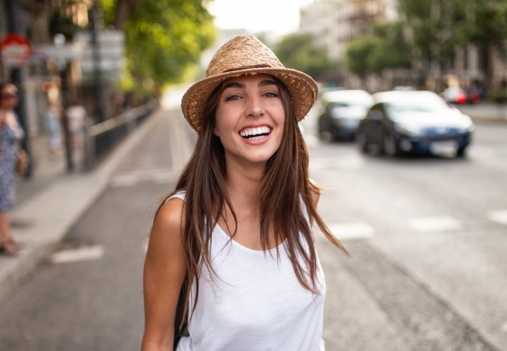 Young woman in sunhat smiling on city sidewalk after direct bonding in Saint Peters