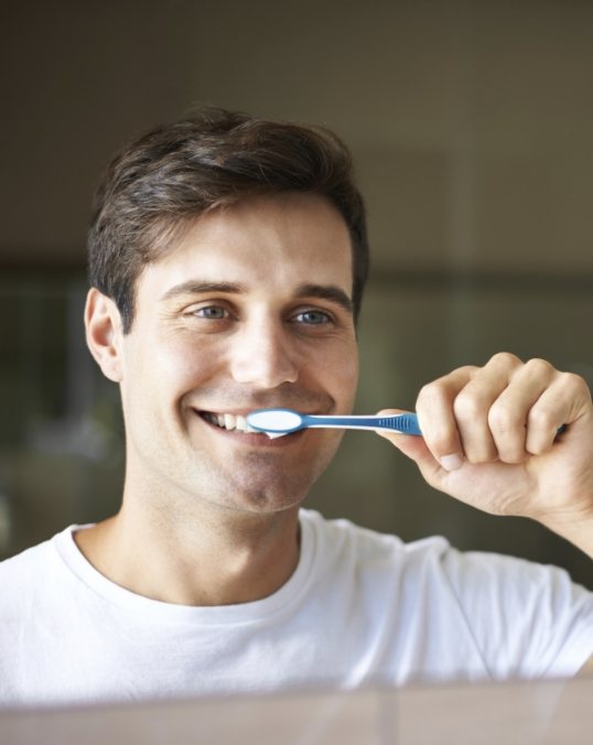 Smiling man brushing his teeth in front of mirror