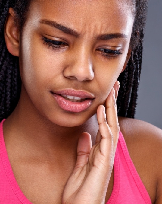 Woman in pink tank top holding side of face in pain