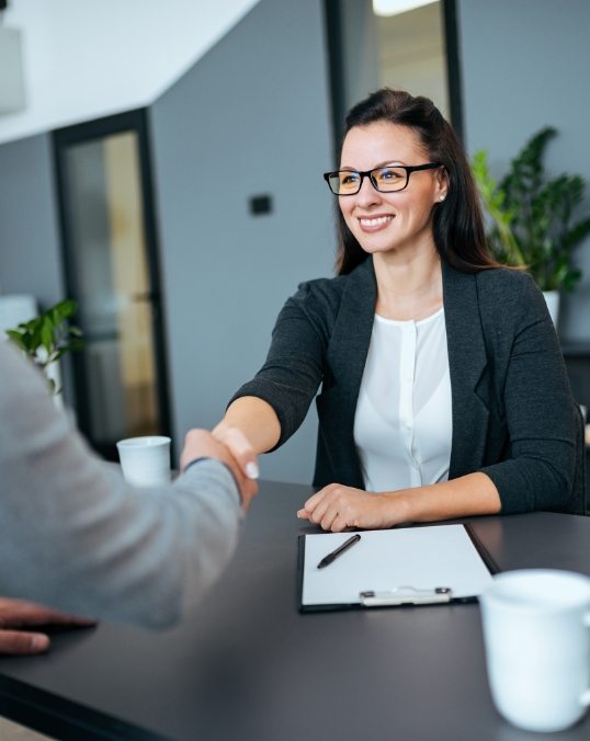 Woman in business attire shaking hands with person across desk