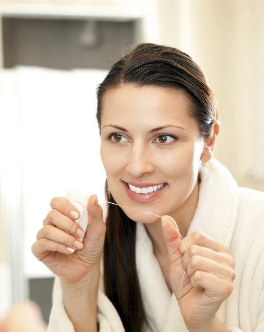 Woman in white bathrobe holding a string of dental floss