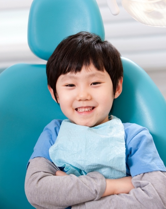 Young smiling boy in light blue shirt crossing his arms in dental chair