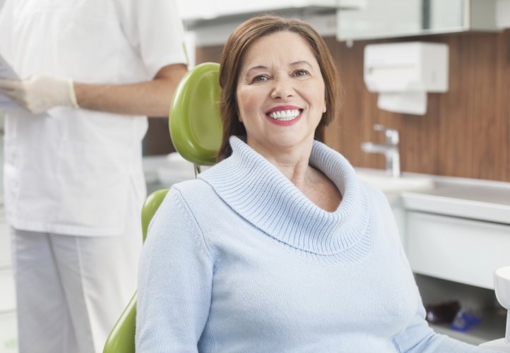 Senior woman in light blue sweater smiling in dental chair