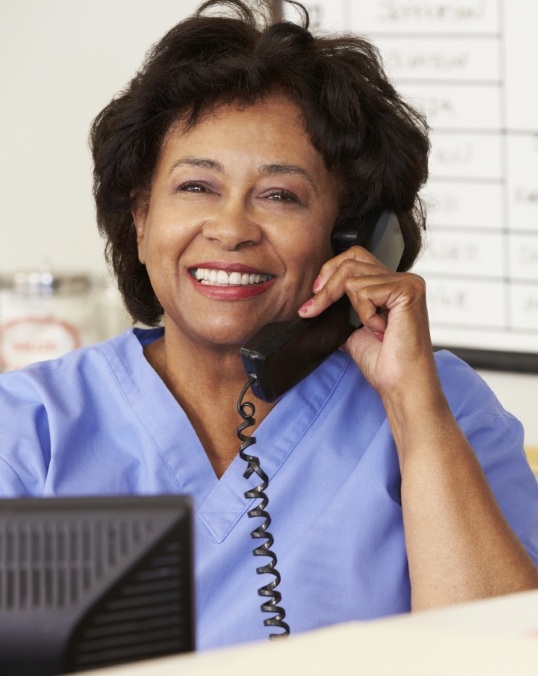 Smiling dental team member in light blue scrubs talking on phone
