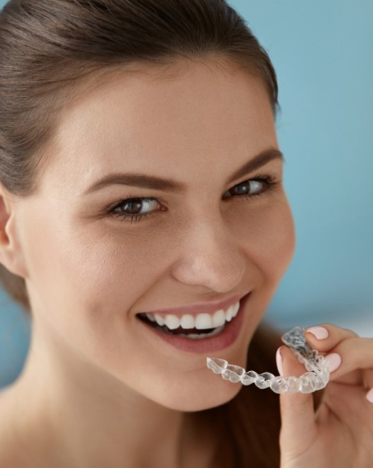 Smiling woman with ponytail holding an Invisalign aligner