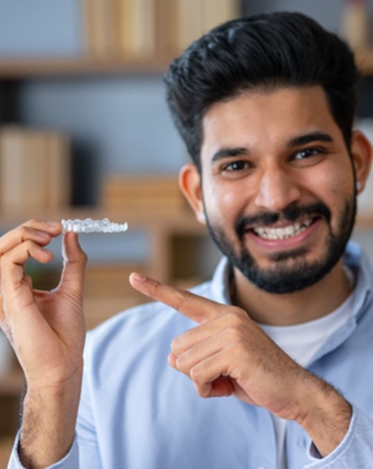 Man in blue shirt smiling while pointing Invisalign aligner