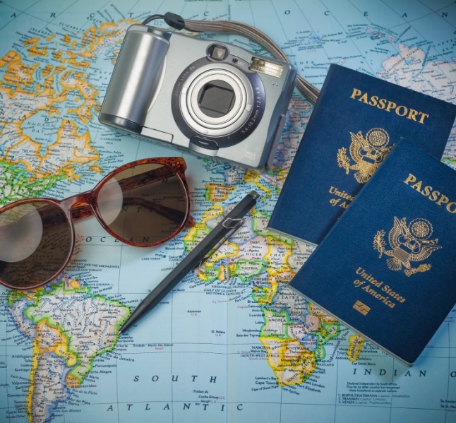 Camera pen sunglasses and two passports laying on a world map