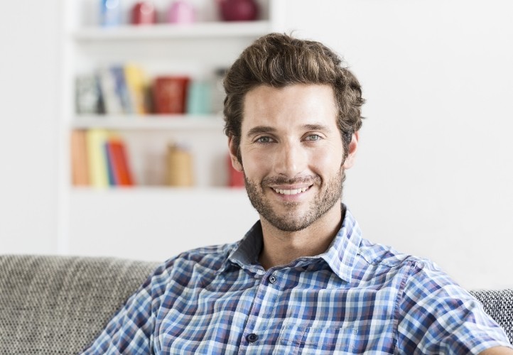 Man in blue plaid shirt smiling on couch after gum disease treatment in Saint Peters