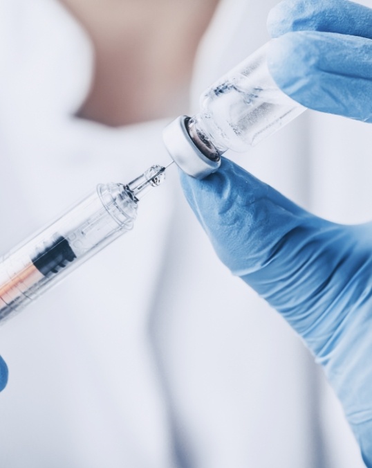 Medical professional drawing clear liquid from a vial into a syringe