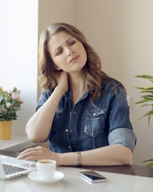 Woman sitting at desk while holding her neck in pain