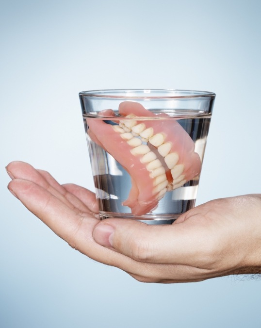 Person holding a glass of water where a set of dentures are soaking