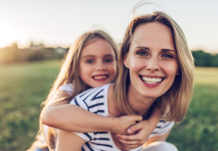 Smiling mother giving daughter piggyback ride after requesting a dental appointment in Saint Peters