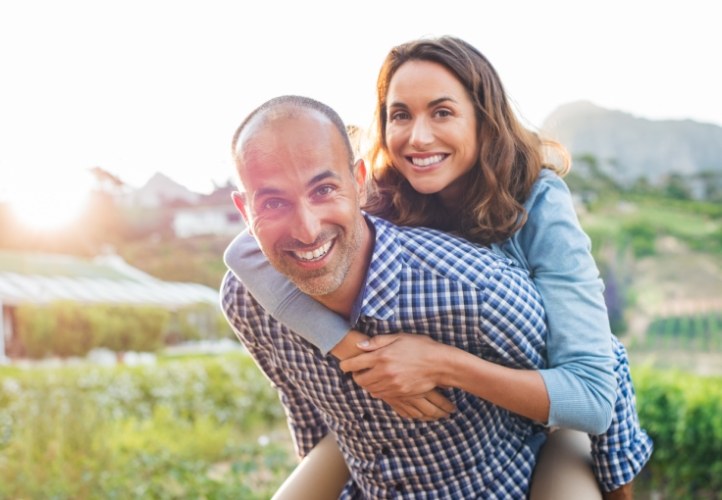 Man giving woman piggyback ride outdoors after restorative dentistry in Saint Peters