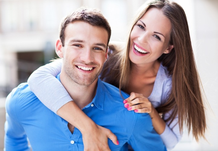 Man and woman grinning outdoors after smile makeover in Saint Peters