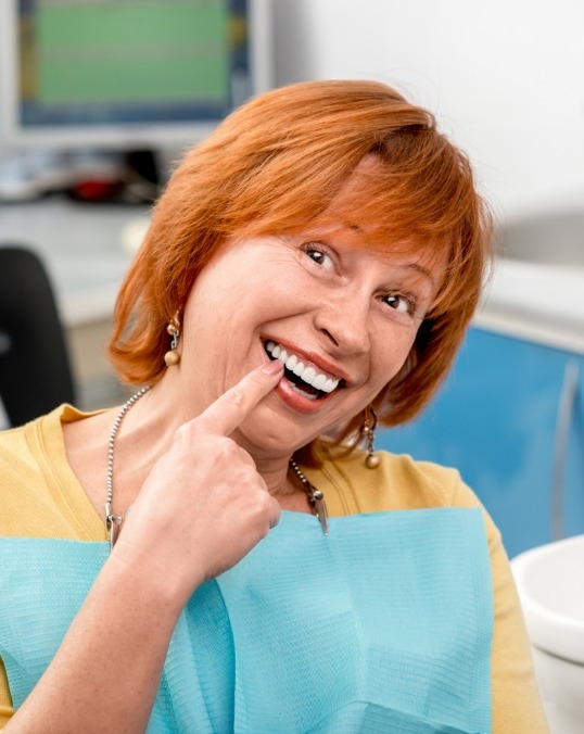Older woman in dental chair pointing to her smile