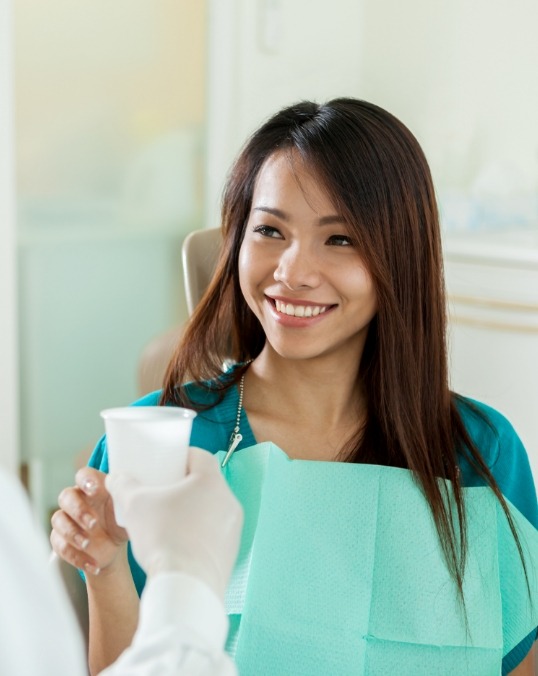 Young woman smiling while dentist hands her a cup of water