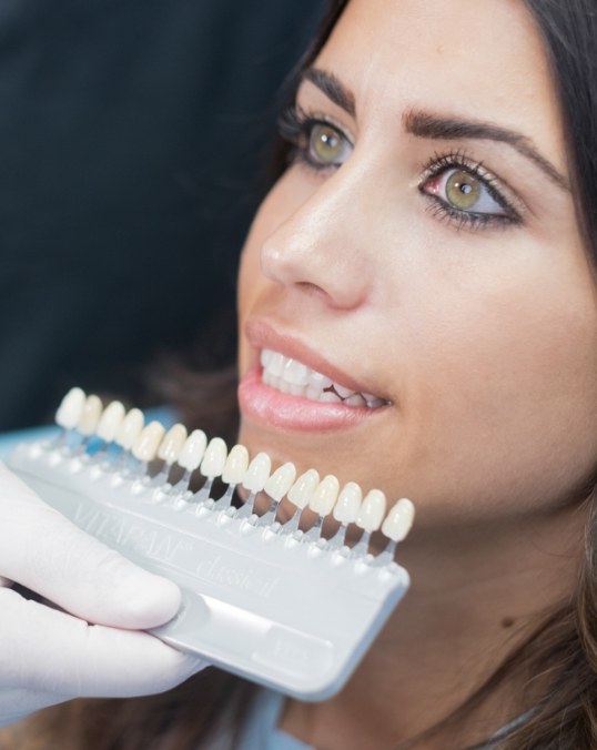 Cosmetic dentist holding a row of veneers in front of woman's smile