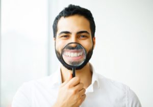 man in white shirt holding magnifying glass to his smile 