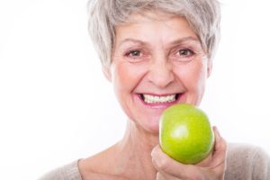 Older woman with dental implants holding an apple.
