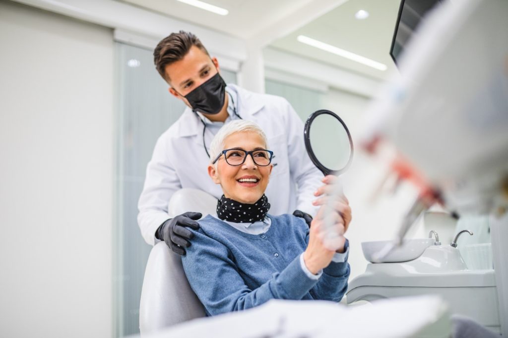 Senior woman smiling in mirror at dentist's office